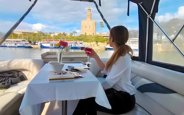 Tourist on Guadalquivir River Cruise enjoying view of Torre del Oro with tapas and drink.