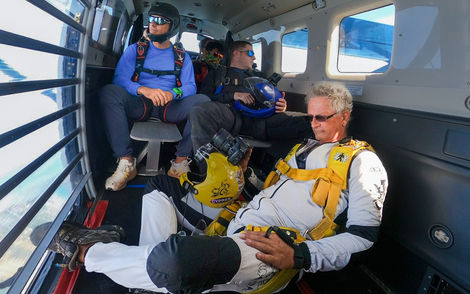 Tourists seated inside a skydiving plane wearing safety gear.