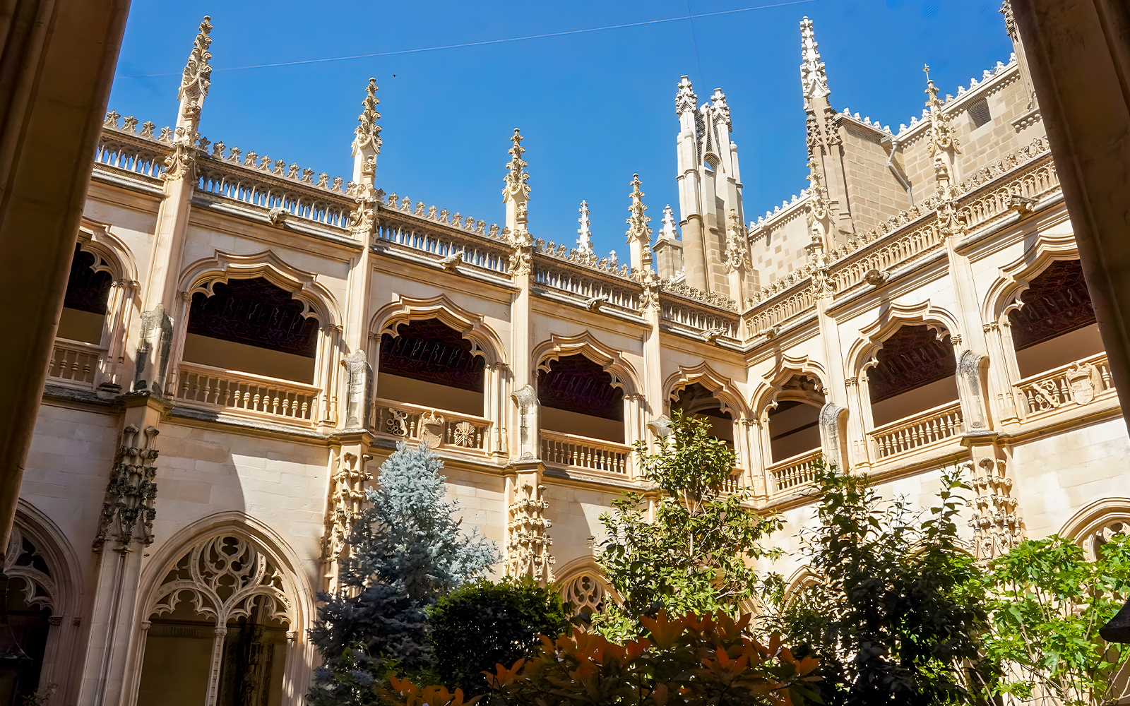 Courtyard view of Monastery of San Juan de los Reyes with Gothic arches and greenery.