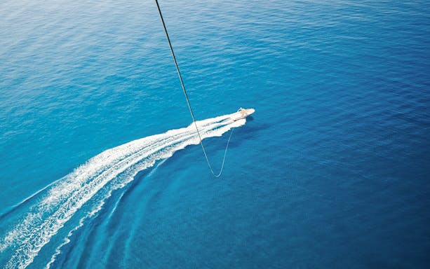Parasailing over the ocean in Albufeira with a speedboat below.