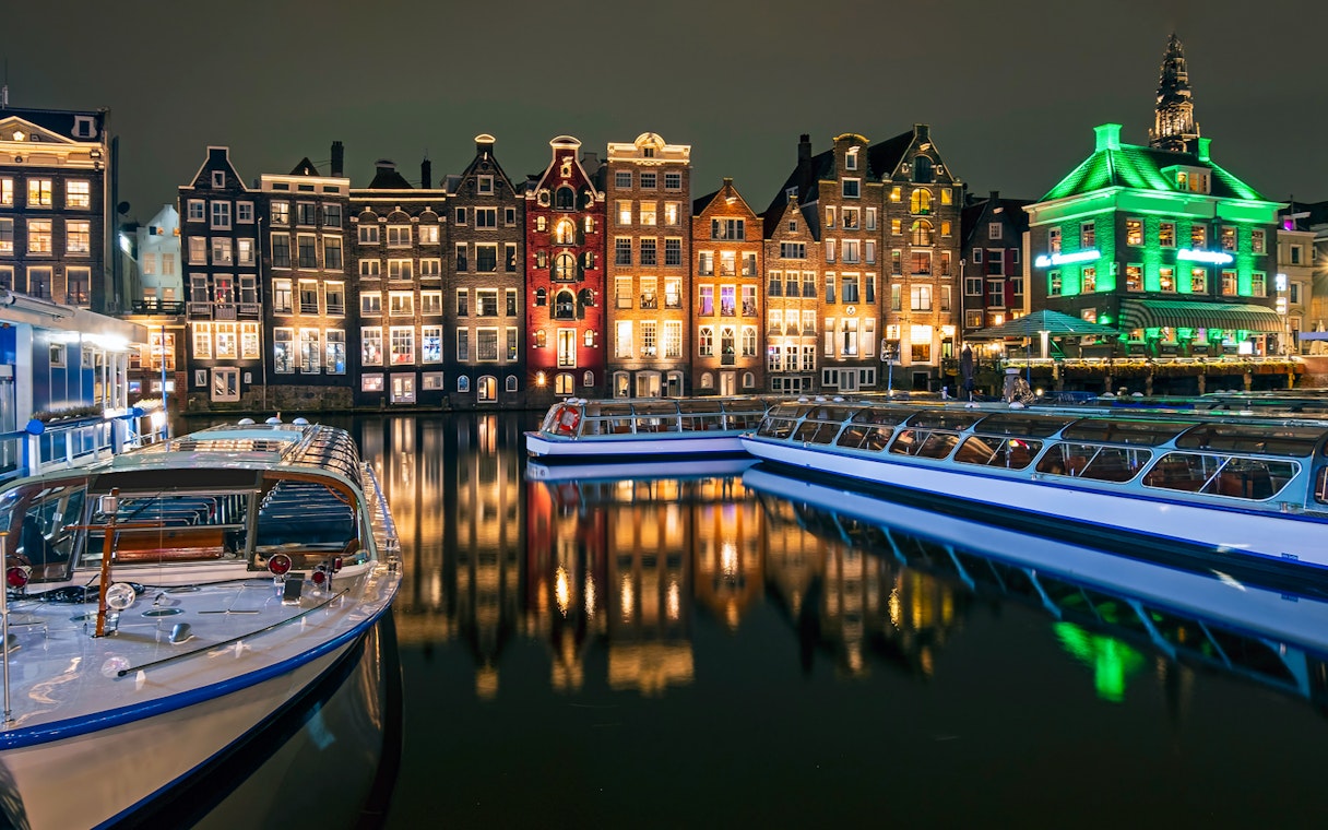 Amsterdam canal boats with illuminated historic buildings at night.