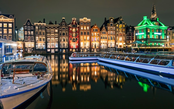 Amsterdam canal boats with illuminated historic buildings at night.