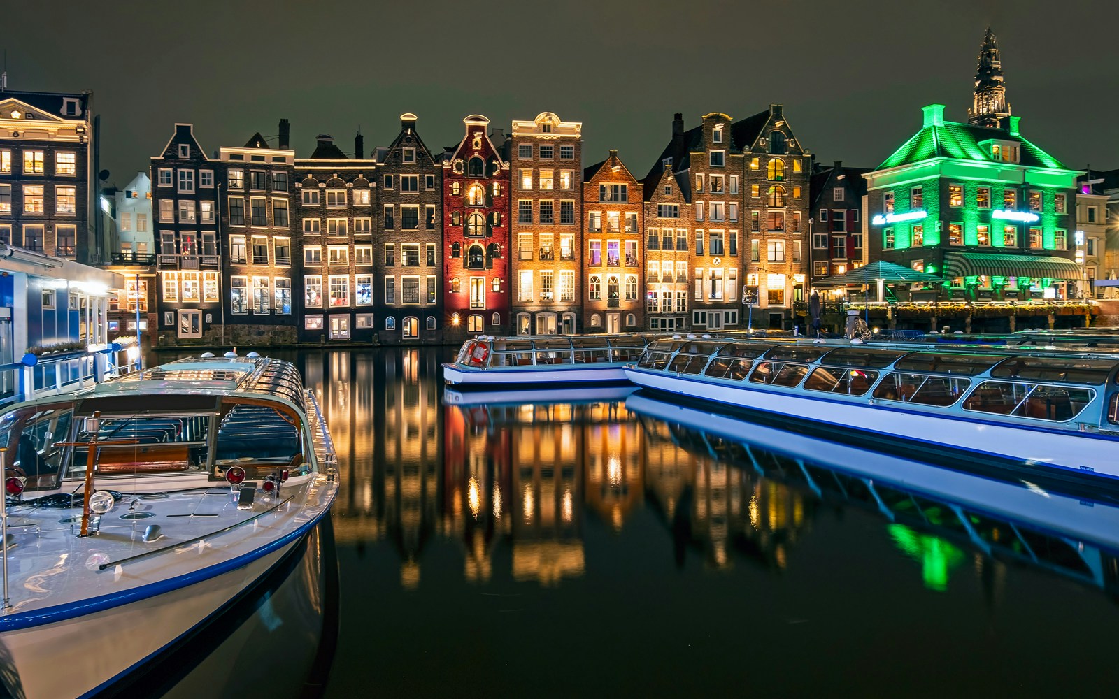 Amsterdam canal cruise boat on water during evening with city lights reflecting.