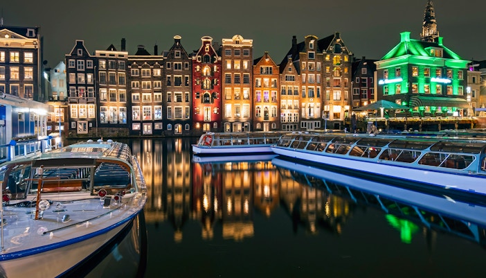 Amsterdam canal boats with illuminated historic buildings at night.
