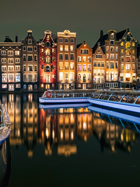 Amsterdam canal boats with illuminated historic buildings at night.