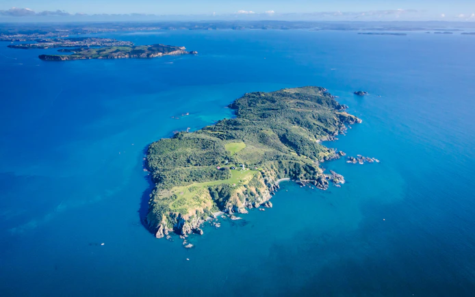 Aerial view of Tiritiri Matangi Island surrounded by blue ocean, accessible by ferry from Auckland.