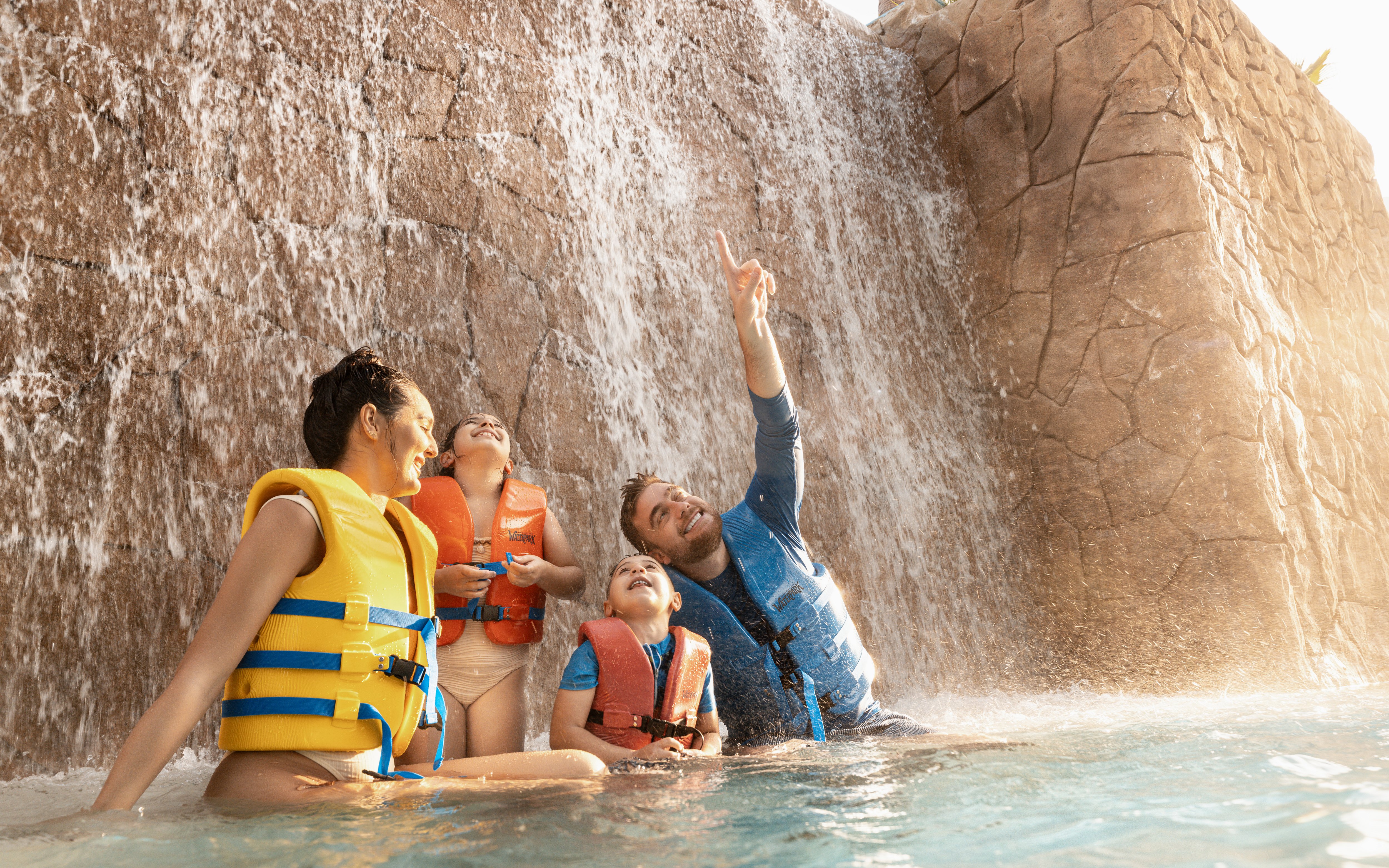 Family enjoying waterfall at Grand Hyatt waterpark, Dubai.