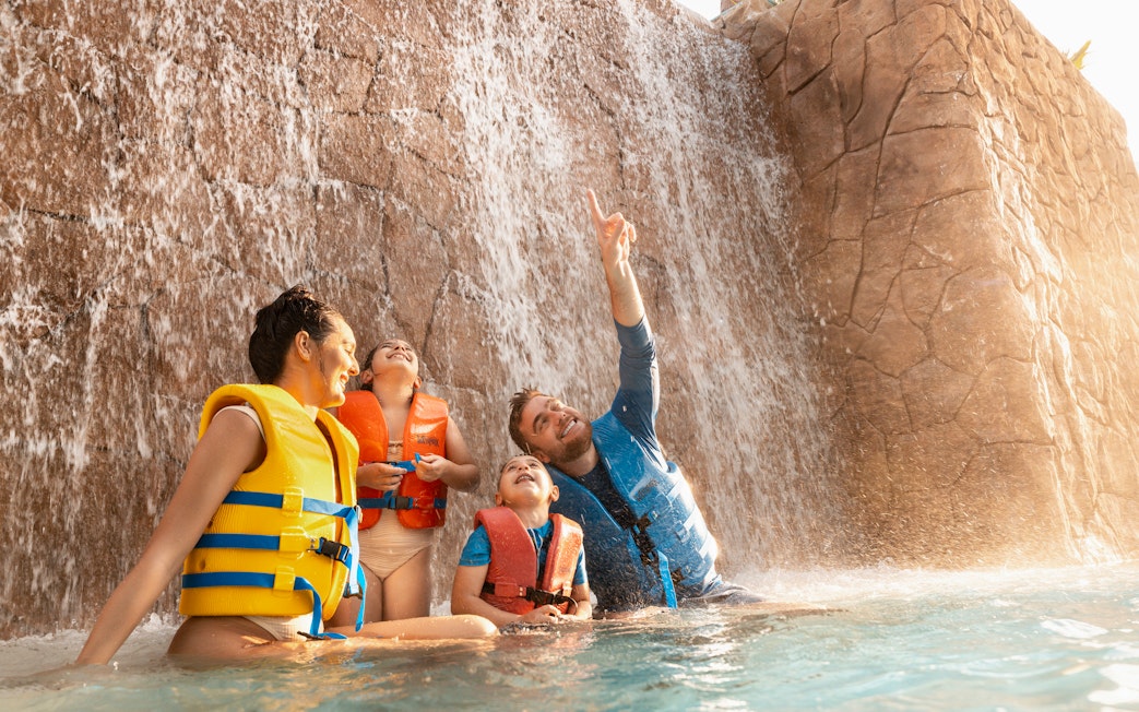Family enjoying waterfall at Grand Hyatt waterpark, Dubai.