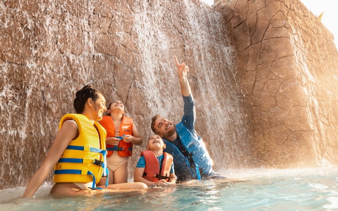 Family enjoying waterfall at Grand Hyatt waterpark, Dubai.
