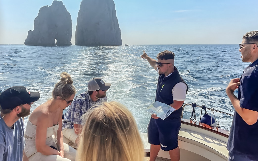 Tour group on a boat near Faraglioni rocks, Capri, with guide explaining the sights.