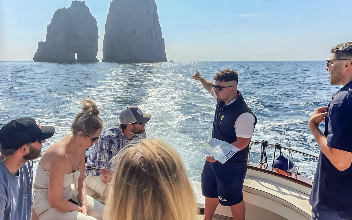 Tour group on a boat near Faraglioni rocks, Capri, with guide explaining the sights.