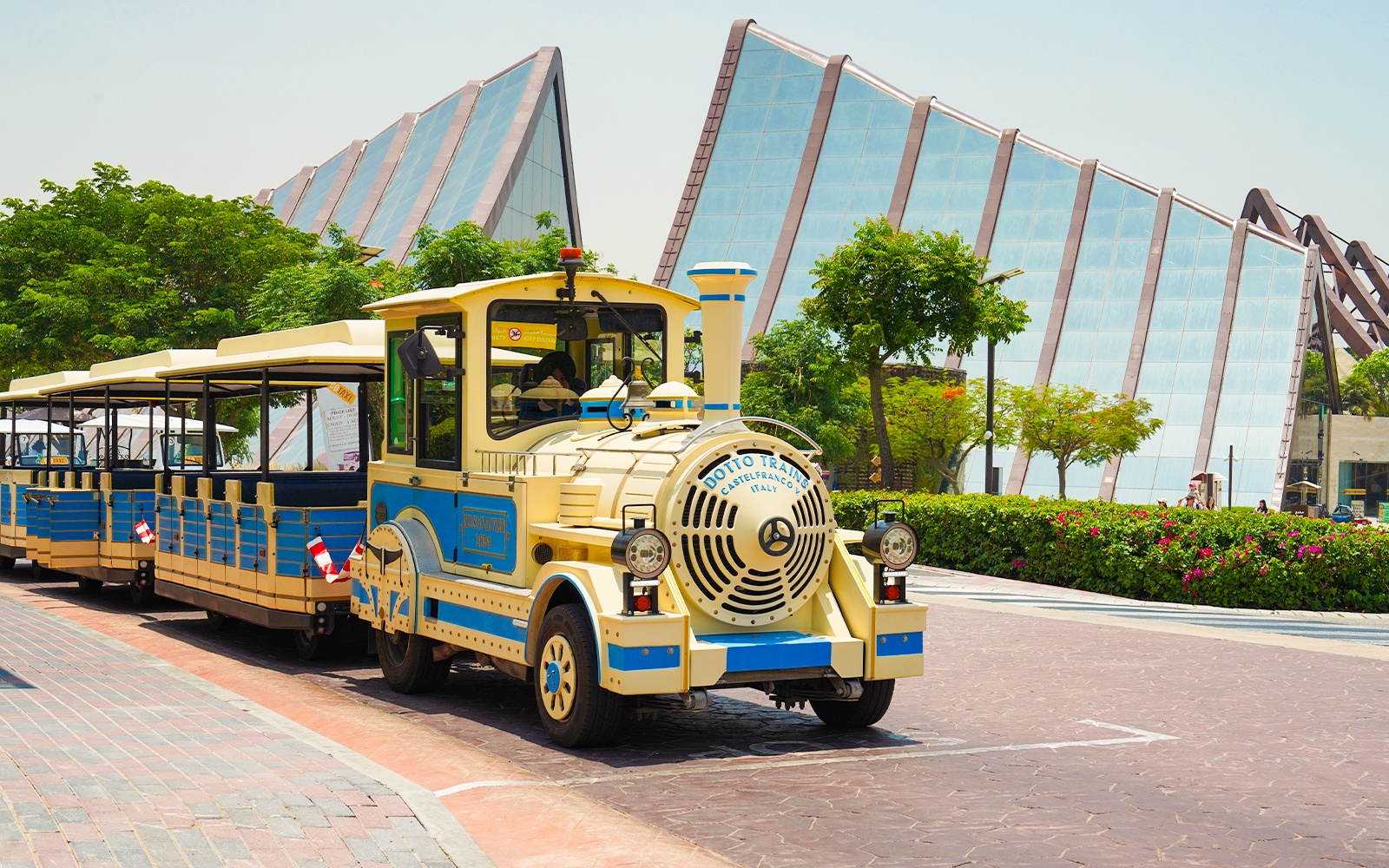 Dubai Safari Park shuttle train in front of modern glass building.