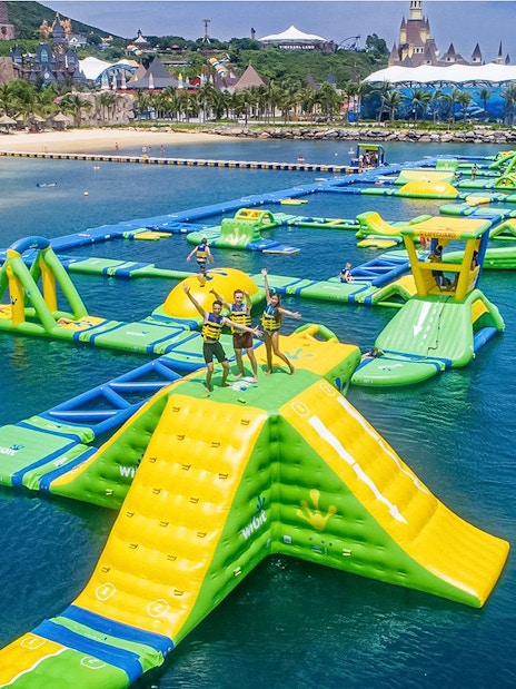 Floating water park with slides and obstacles at Splash Bay, featuring people enjoying activities.