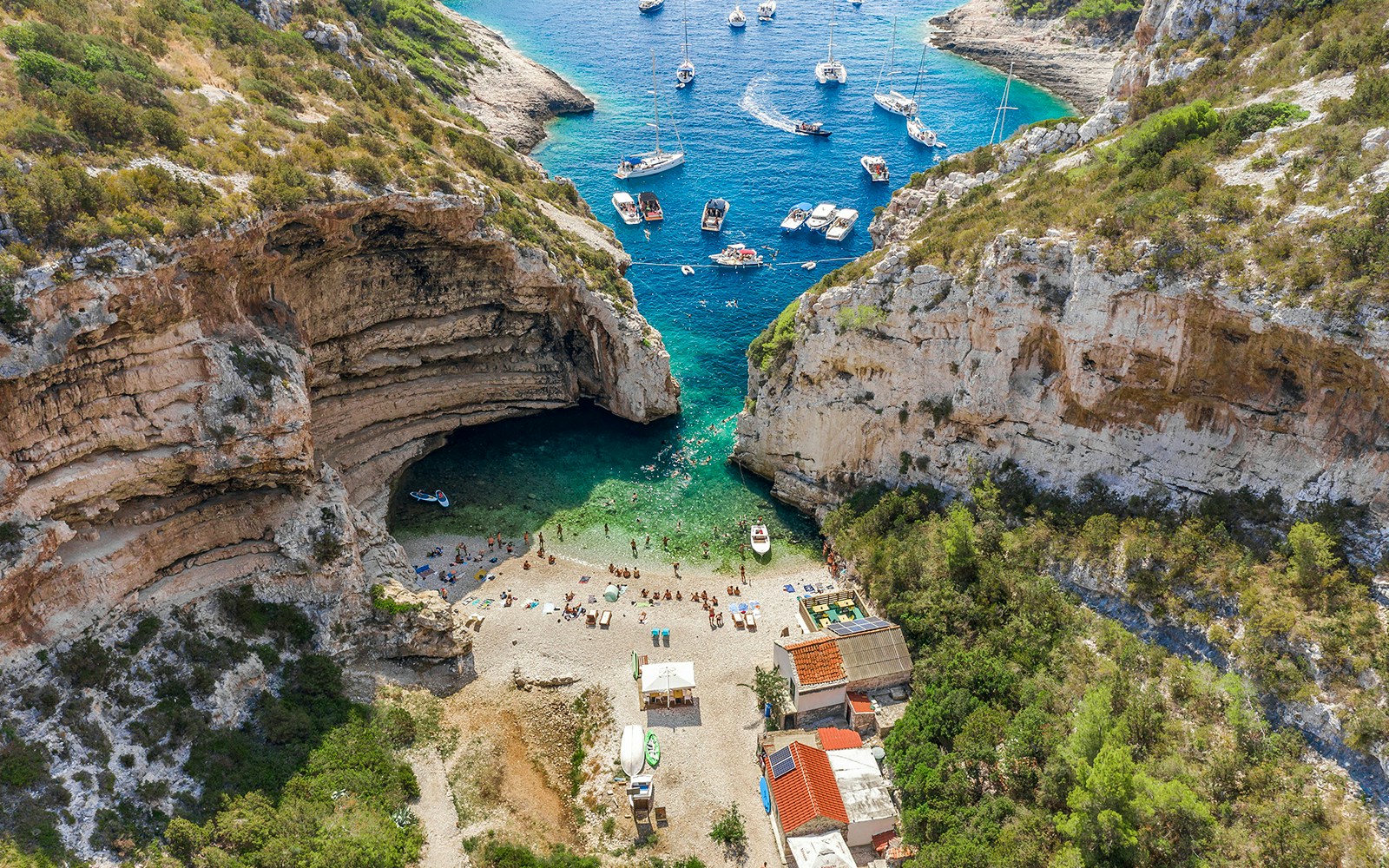 Aerial view of Stiniva Cove beach with boats and visitors on Vis Island, Croatia.
