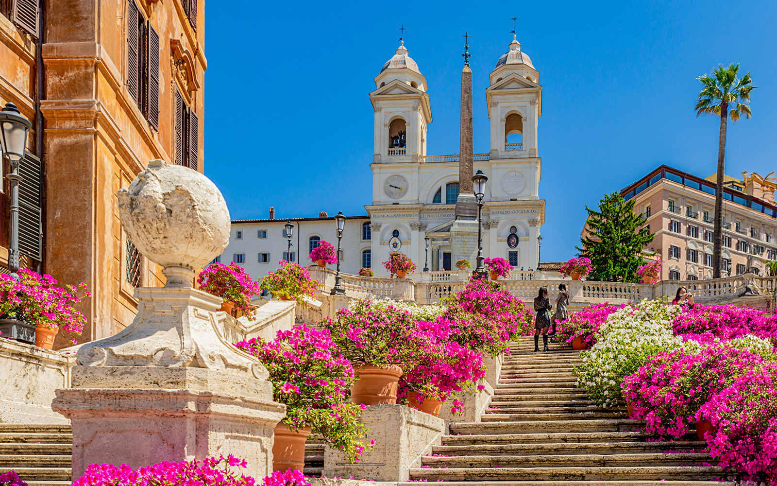 Spanish Steps panorama with Trinita dei Monti church, obelisk, blue sky, clouds, and azaleas in Rome, Italy.