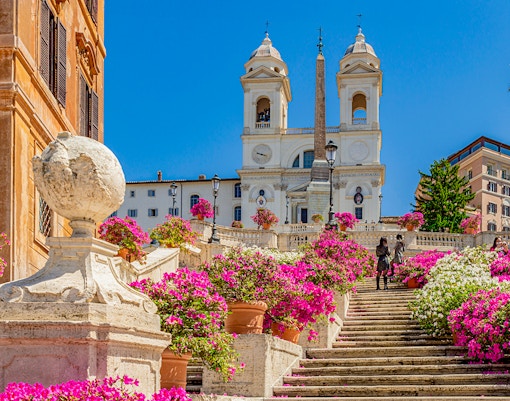 Spanish Steps panorama with Trinita dei Monti church, obelisk, blue sky, clouds, and azaleas in Rome, Italy.