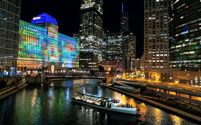Chicago River dinner cruise with city skyline and colorful building lights.