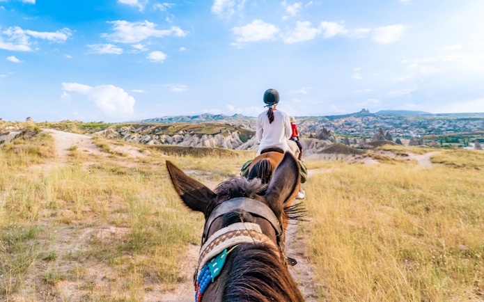 Woman horse riding through Cappadocia's mountain valleys, Turkey.