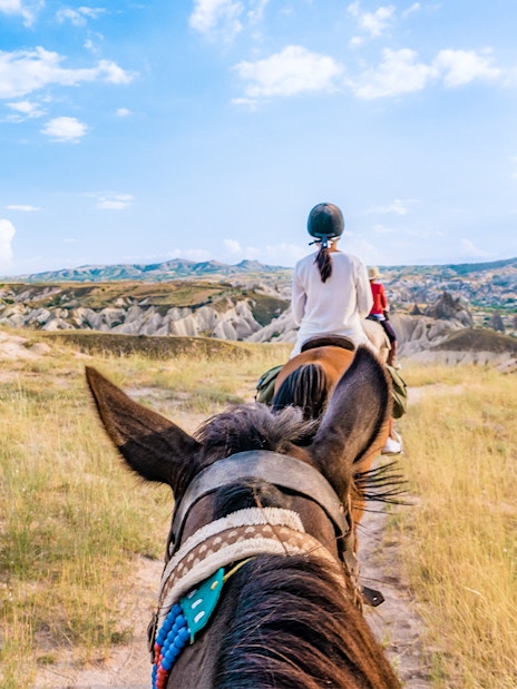 Woman horse riding through Cappadocia's mountain valleys, Turkey.