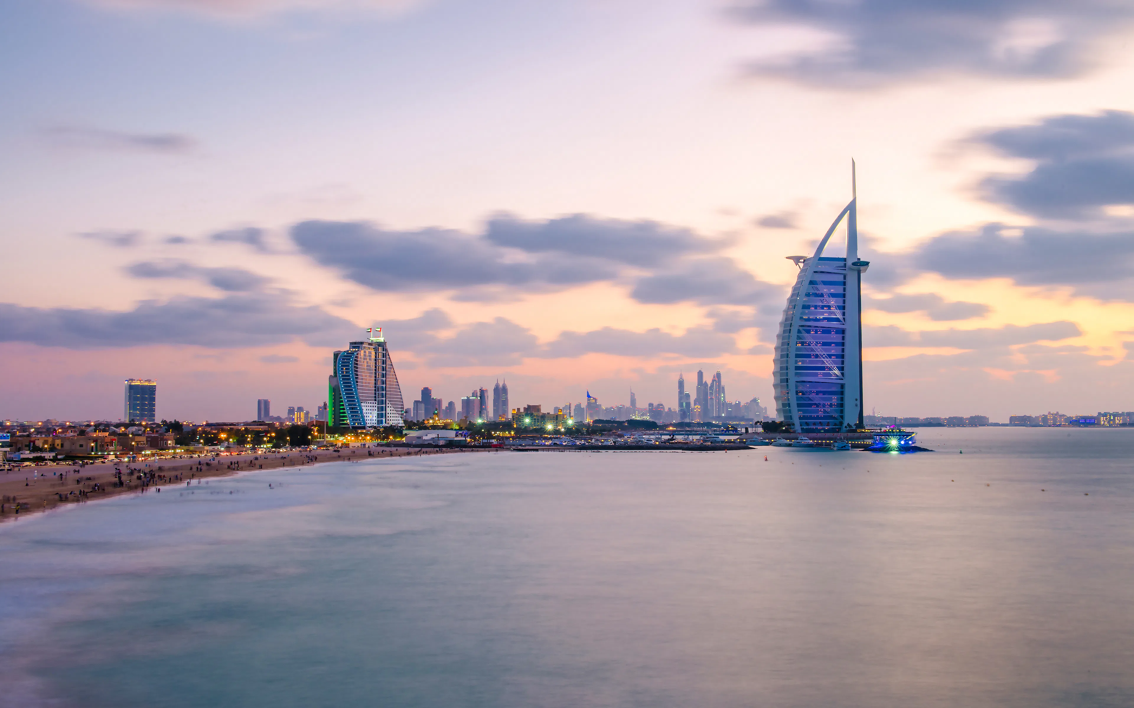 Burj Al Arab and Jumeirah Beach Hotel at sunset, Dubai skyline in the background.