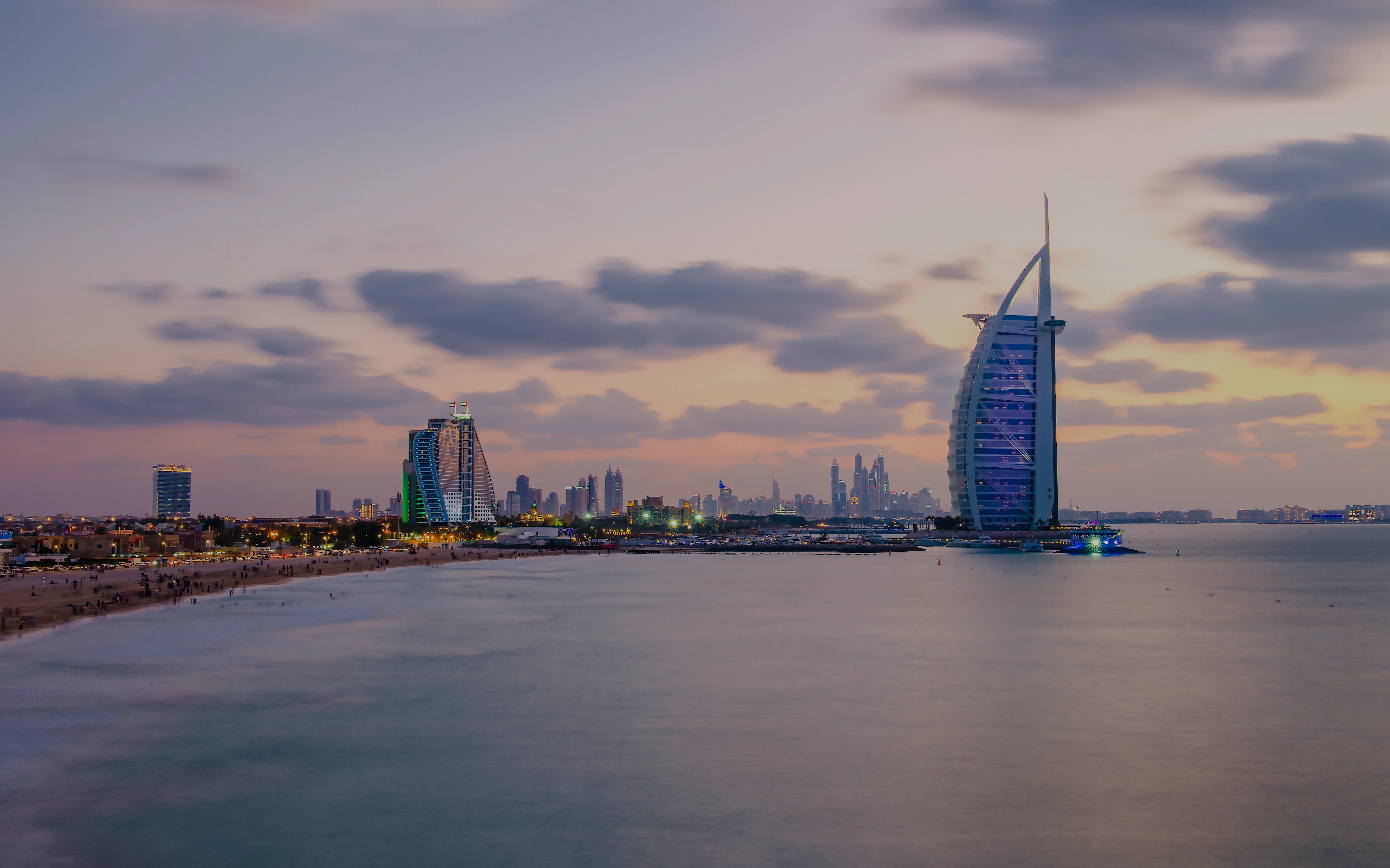 Burj Al Arab and Jumeirah Beach Hotel at sunset, Dubai skyline in the background.