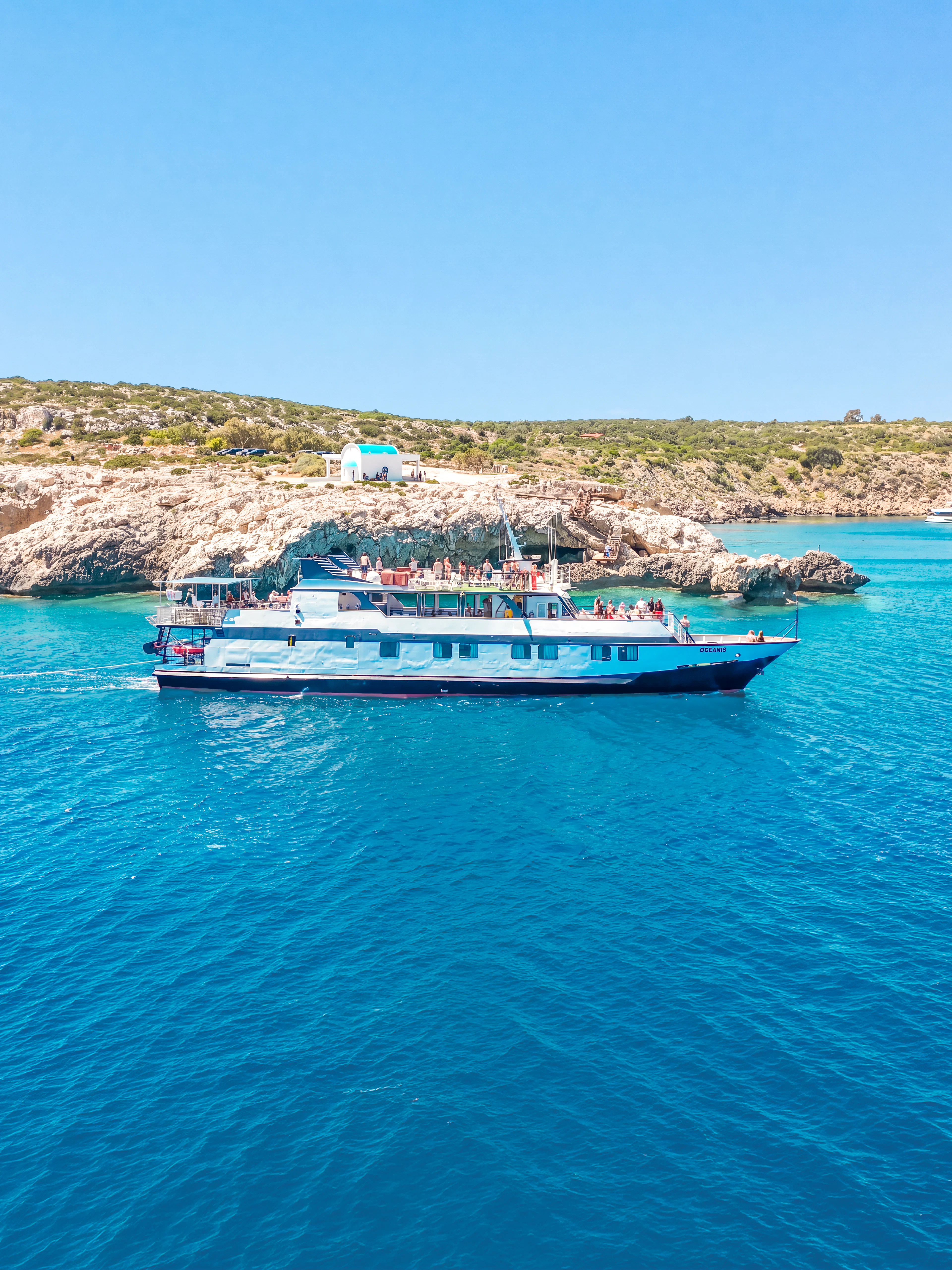 Cruise ship sailing near rocky coastline on Blue Lagoon tour from Larnaca.