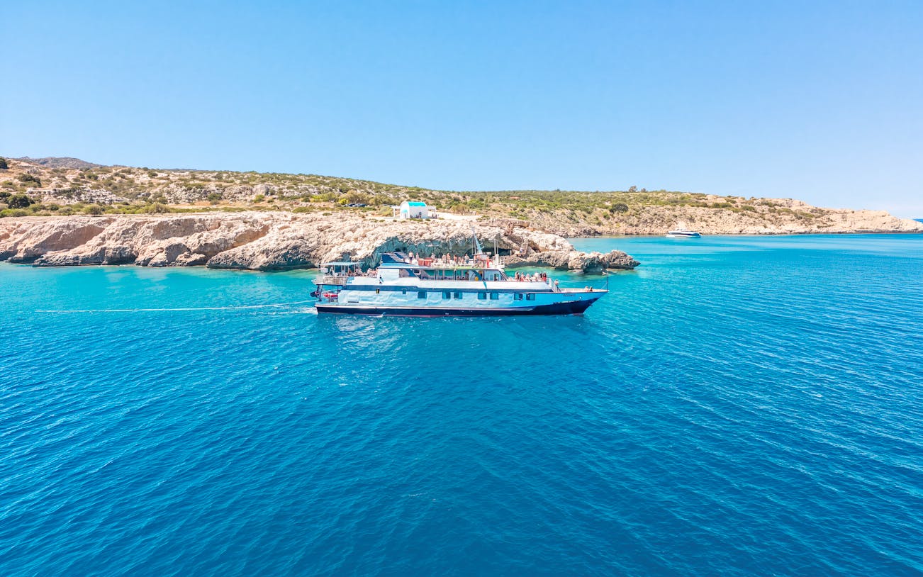 Cruise ship sailing near rocky coastline on Blue Lagoon tour from Larnaca.
