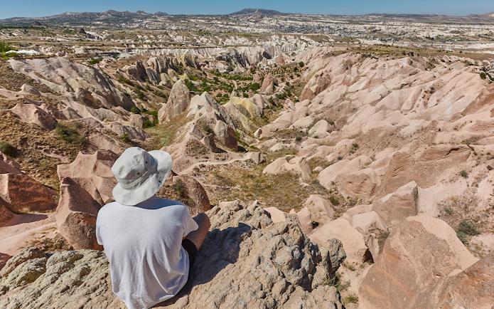 Person sitting on a rock overlooking the unique rock formations at Goreme Open Air Museum, Cappadocia.