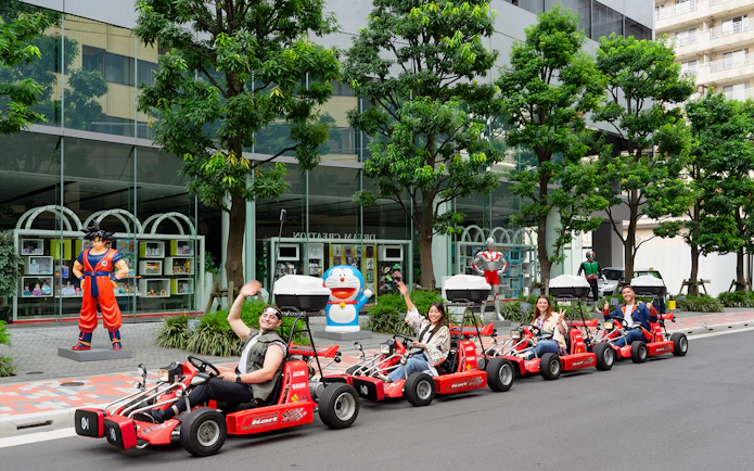 People enjoying Akihabara GoKart Experience in Tokyo, driving past anime statues.