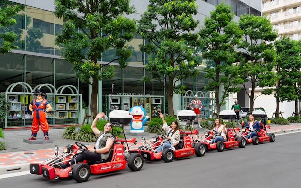 People enjoying Akihabara GoKart Experience in Tokyo, driving past anime statues.