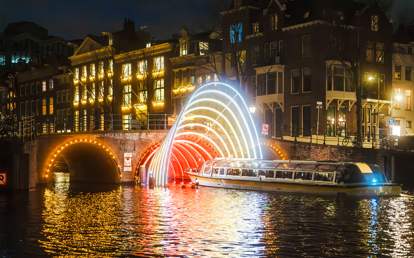 Canal cruise passing under illuminated arches during Amsterdam Light Festival.
