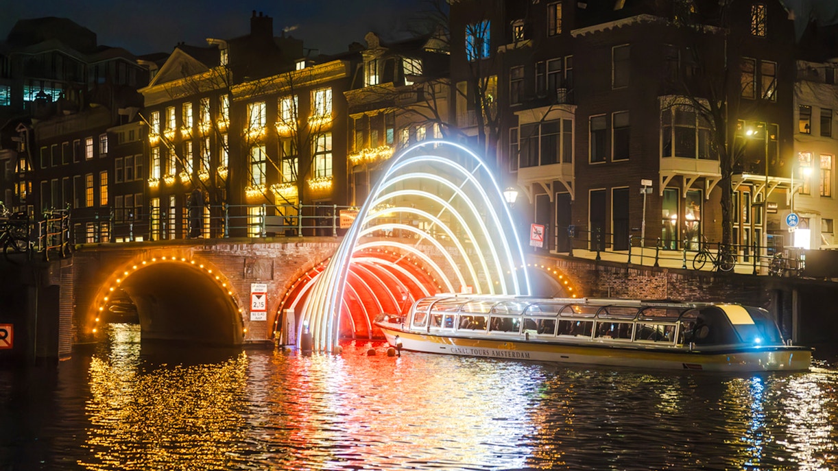 Canal cruise passing under illuminated arches during Amsterdam Light Festival.