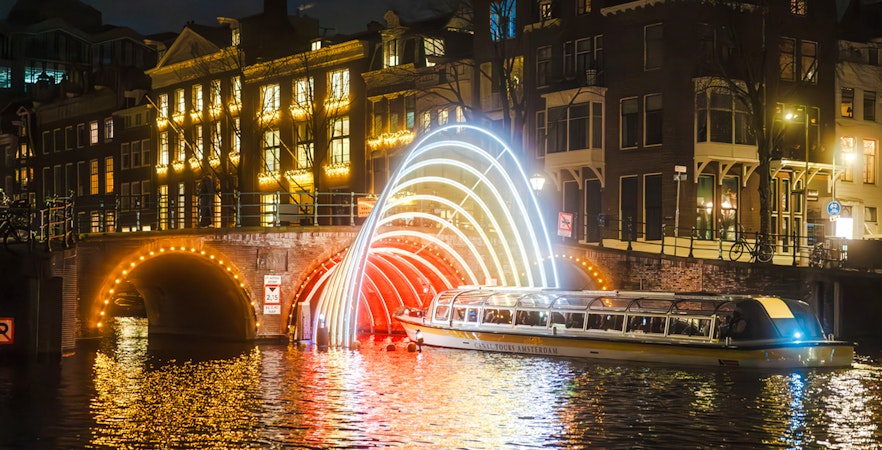 Canal cruise passing under illuminated arches during Amsterdam Light Festival.