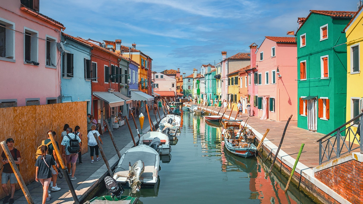 Colorful houses in Burano with people strolling along the canal, Venice, Italy.