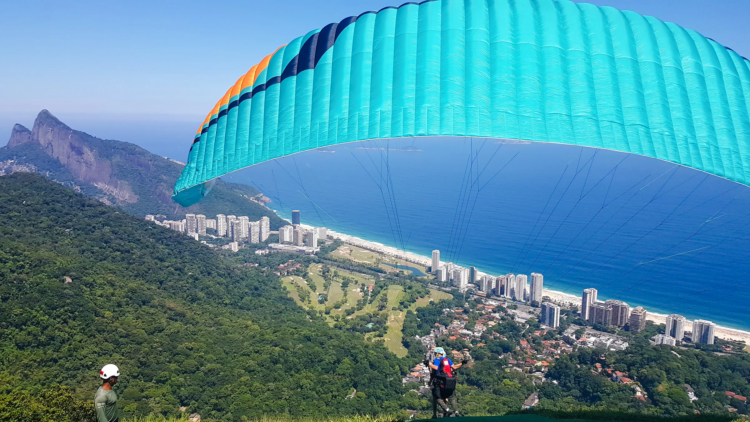 Tandem paragliding over São Conrado Beach, Rio de Janeiro, with cityscape and ocean view.