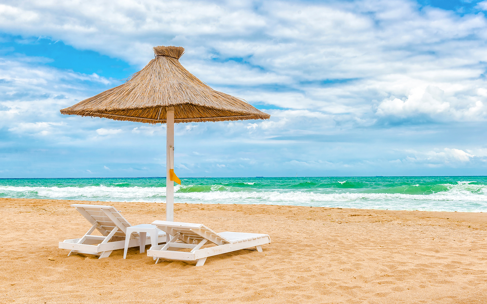 Sun loungers under a thatched umbrella on Mamaia Beach, Constanta, Romania.
