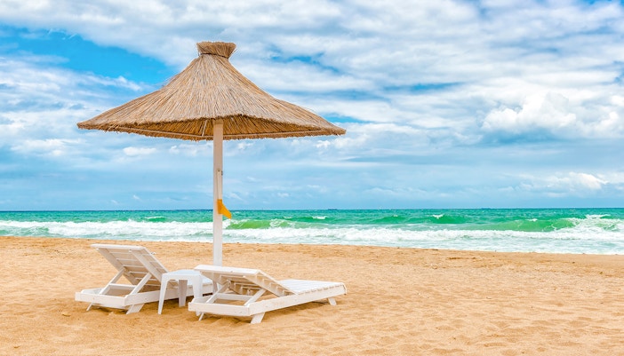 Sun loungers under a thatched umbrella on Mamaia Beach, Constanta, Romania.