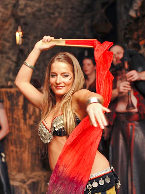 Bellydancer performing at a medieval dinner show with musicians in the background.