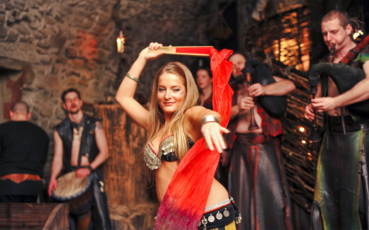 Bellydancer performing at a medieval dinner show with musicians in the background.