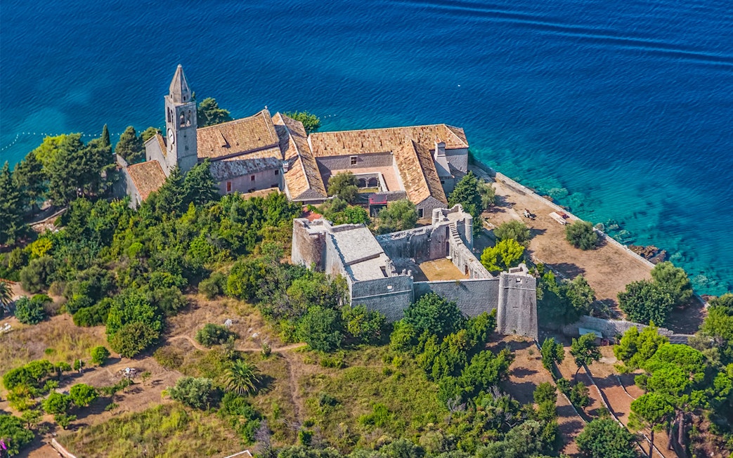 Aerial view of a historic monastery on the Elaphiti Islands near Dubrovnik, surrounded by lush greenery and blue sea.