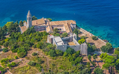 Aerial view of a historic monastery on the Elaphiti Islands near Dubrovnik, surrounded by lush greenery and blue sea.
