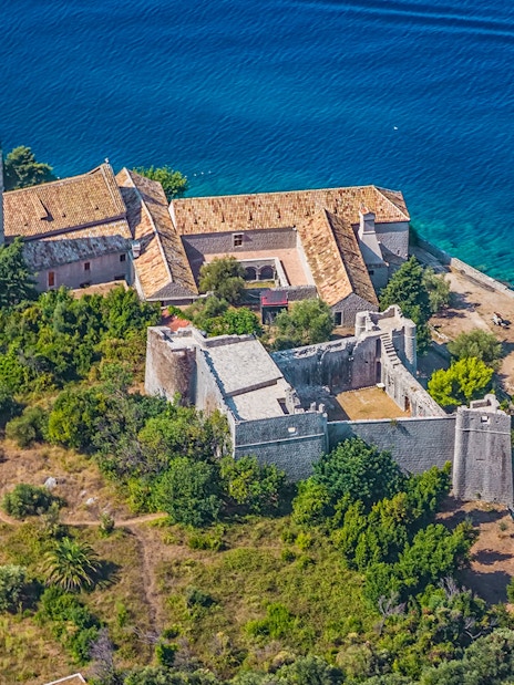 Aerial view of a historic monastery on the Elaphiti Islands near Dubrovnik, surrounded by lush greenery and blue sea.
