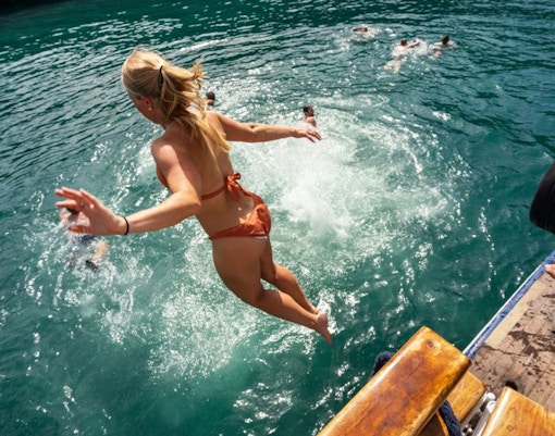 Person jumping into Palea Kameni hot springs from a boat.