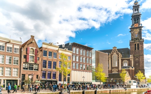 Anne Frank House and Westerkerk tower in Amsterdam with visitors outside.