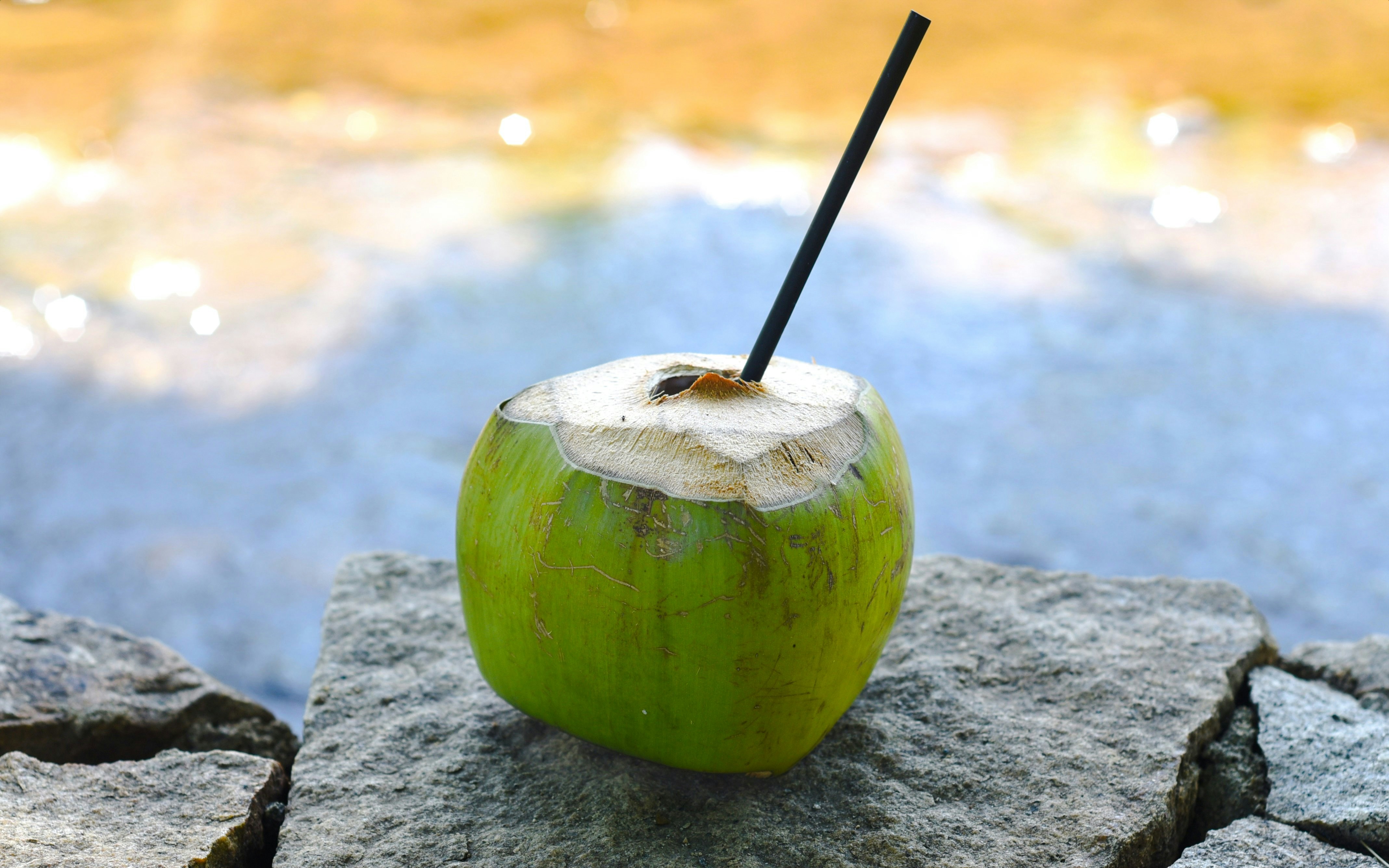 Coconut drink with straw on stone by water.
