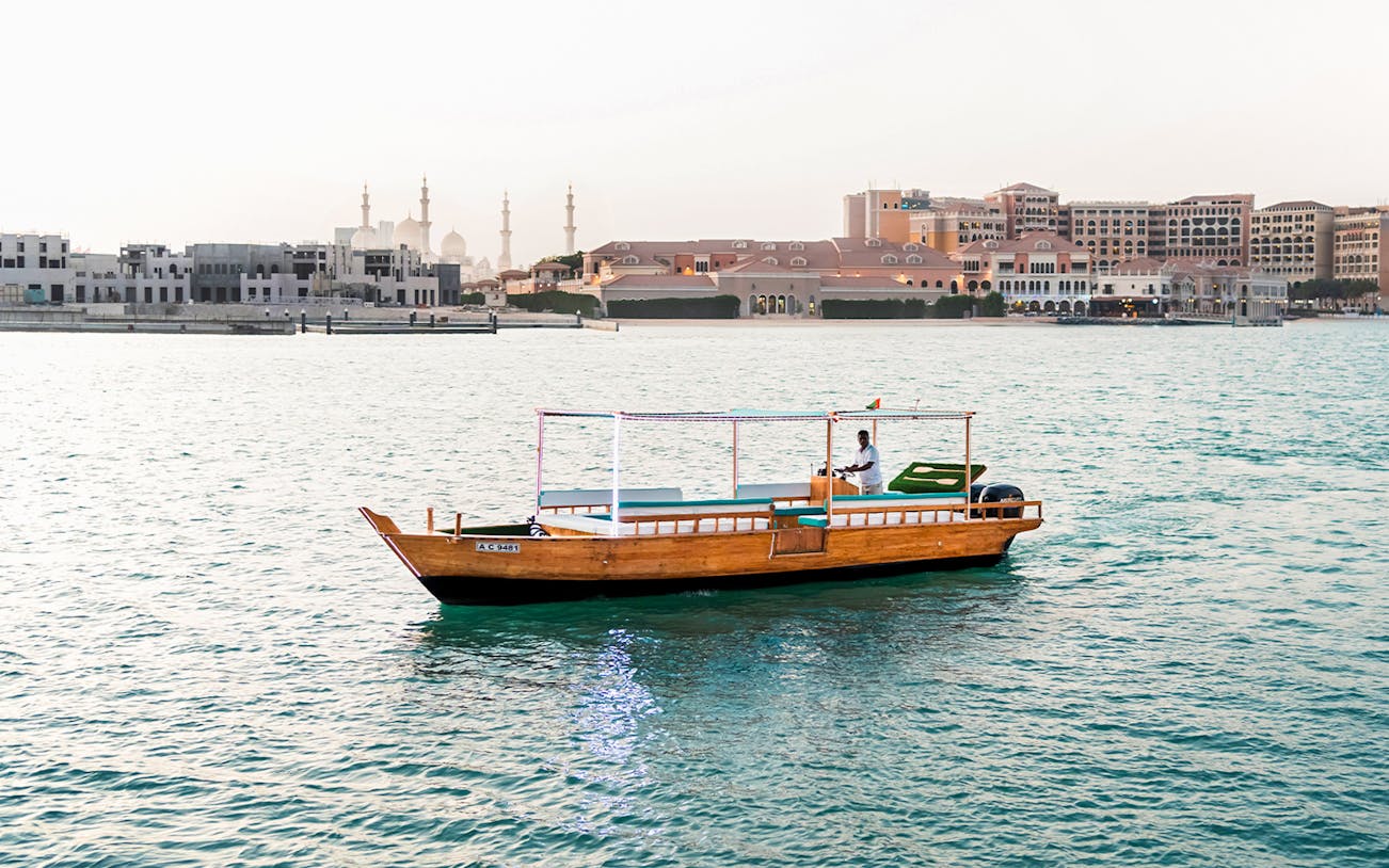 Traditional boat cruising near Abu Dhabi skyline with mosque in background.