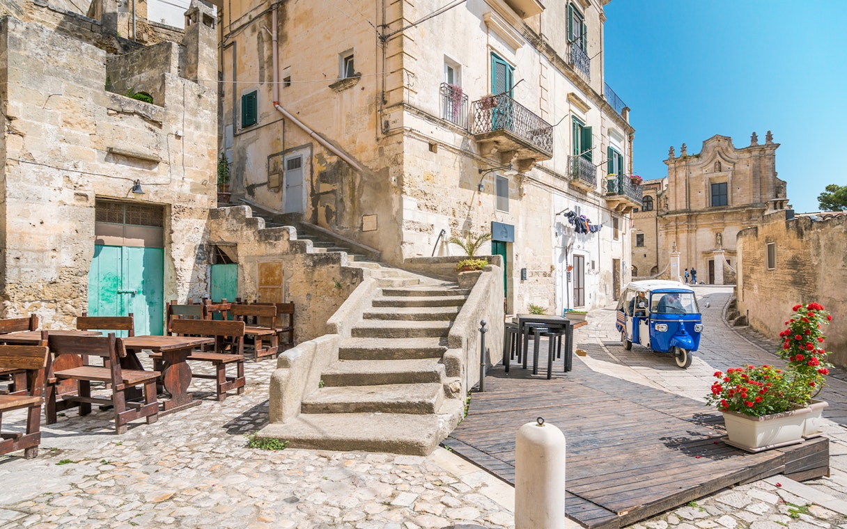 Stone buildings and narrow street with a blue tuk-tuk in Matera, Italy.