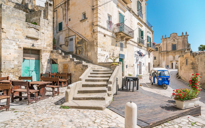 Stone buildings and narrow street with a blue tuk-tuk in Matera, Italy.