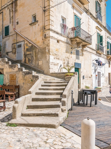 Stone buildings and narrow street with a blue tuk-tuk in Matera, Italy.
