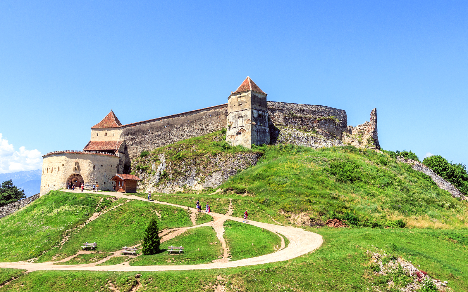 Medieval fortress on a hill with tourists walking, near Bran Castle, Romania.